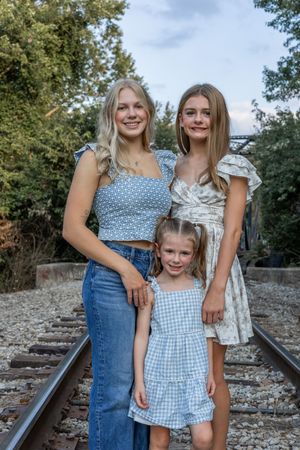 Three people pose together on rustic railroad tracks wearing coordinated blue and white outfits.