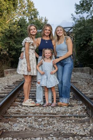 Family group poses together on rocky railroad tracks in coordinated blue and white outfits.