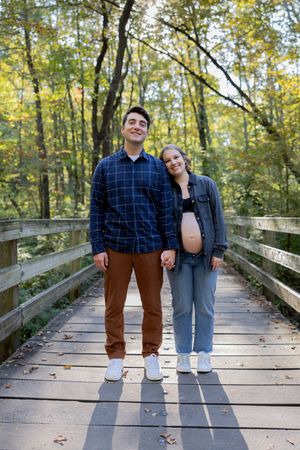 A couple poses playfully on a wooden boardwalk surrounded by autumn trees.
