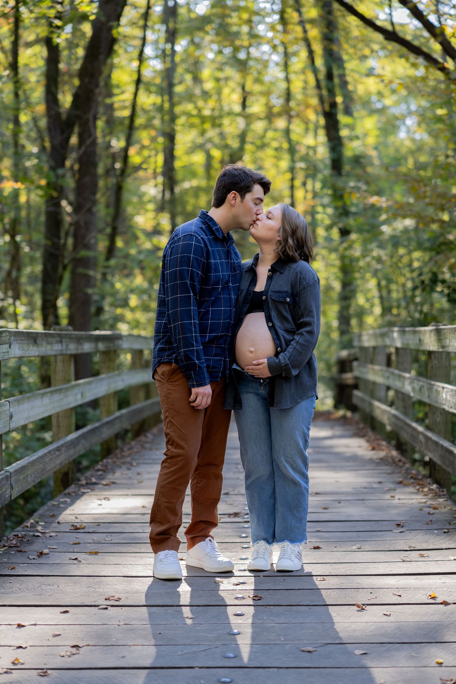A couple shares intimate moments on a wooden boardwalk in a forest setting.
