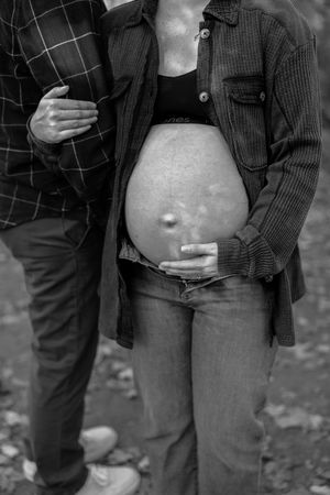 Black and white maternity photos focusing on a pregnant belly with gentle hand placement.