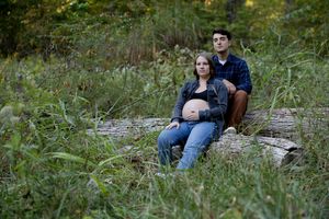 A couple sits together on rocks surrounded by grass and autumn foliage.