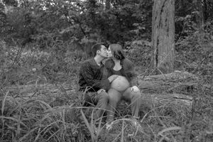 A couple shares an intimate moment together while sitting on fallen logs in a wooded area.