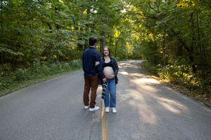 A couple walks hand in hand down a sunlit forest path surrounded by green foliage.
