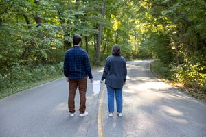 Two people stroll together on a tree-lined path during a sunny afternoon.