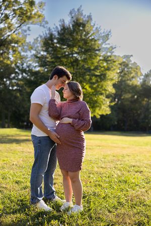 A couple embraces in a sunny field with golden light and green grass.