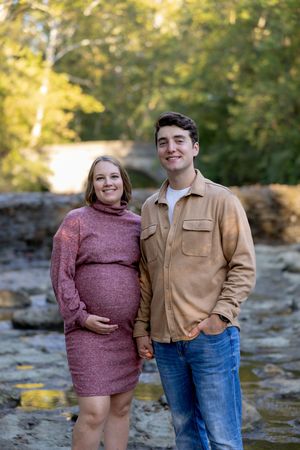A couple poses together on rocky terrain with autumn trees in the background.
