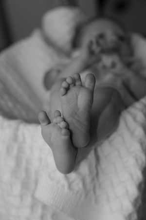 Black and white close-up of tiny baby feet on soft white fabric.