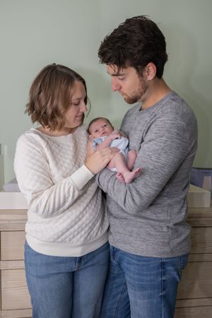 Parents in cozy sweaters hold and gaze lovingly at their newborn.