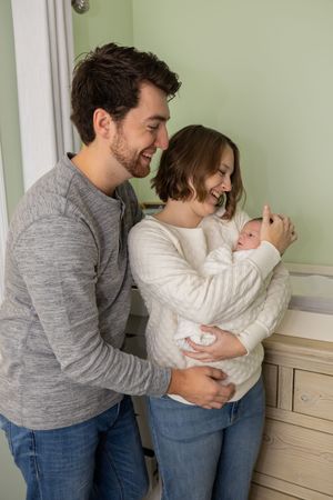 Parents sharing intimate moments with their newborn baby against a light green wall.