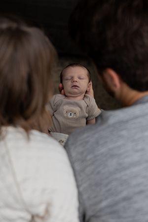 Parents in grey and white sweaters sharing tender moments with their sleeping newborn.