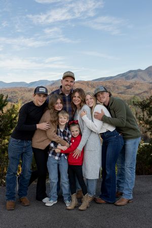 Family group poses together outdoors with mountains and autumn foliage in background.