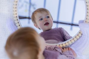 Baby in purple outfit looks down at reflective surface.