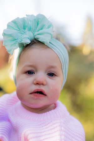 Baby in pink sweater wearing mint green bow headband smiles at camera.