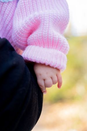 Close-up of baby's hand in pink sweater against dark background.