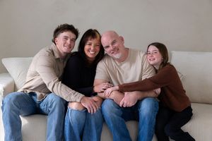 A group of four people sitting close together and laughing on a white couch in a casual indoor setting.