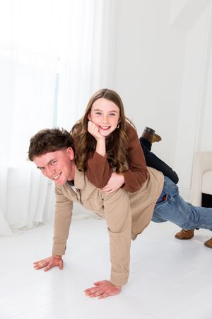 Two people playfully pose in a bright white studio setting with one person giving a piggyback ride.