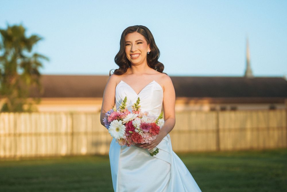A bride in a white dress holds a colorful bouquet while standing on a lawn.