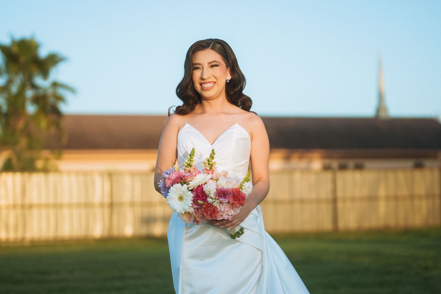 A bride in a white dress holds a colorful bouquet while standing on a lawn.