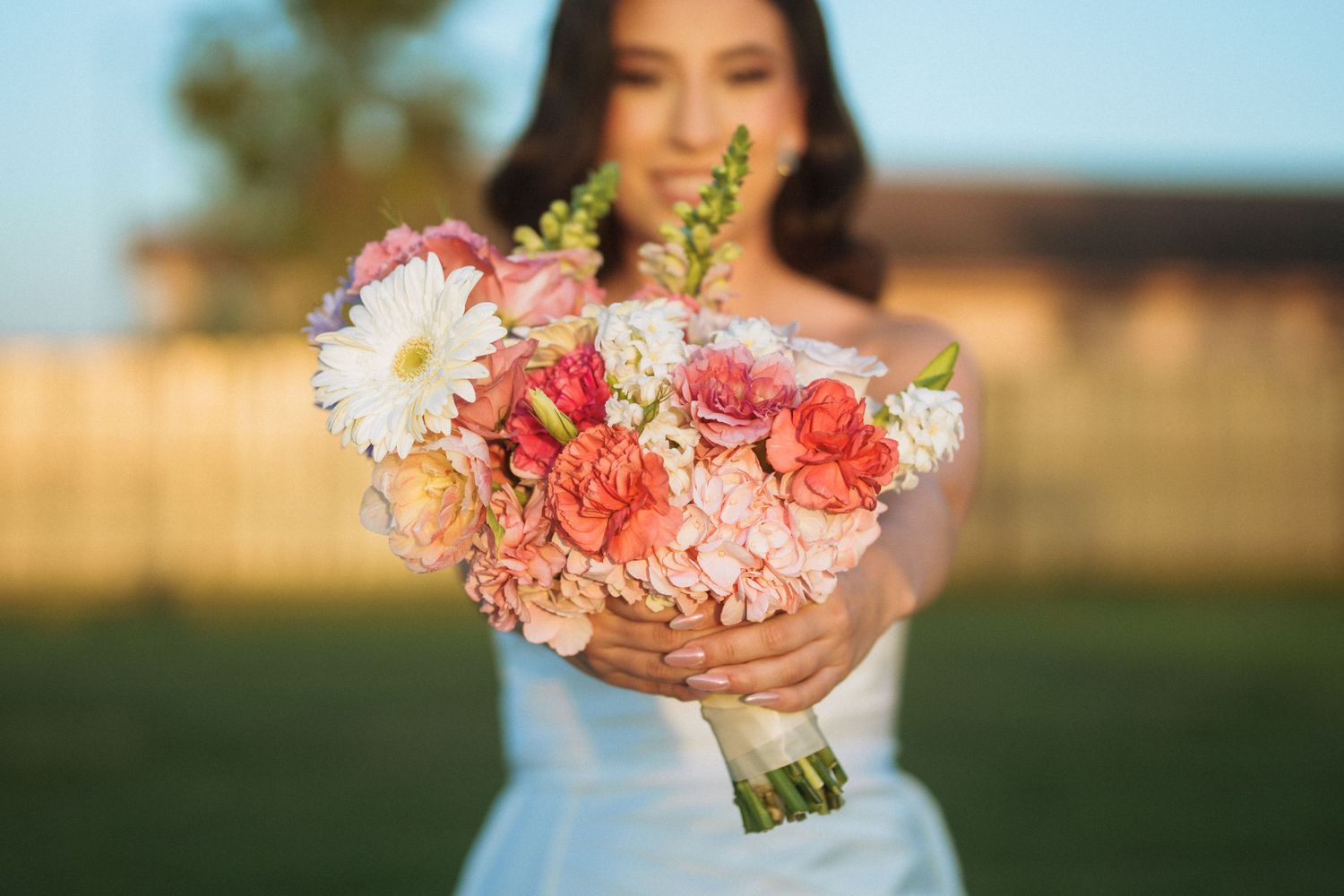 Close-up of a pink and coral wedding bouquet held by someone in a white dress.
