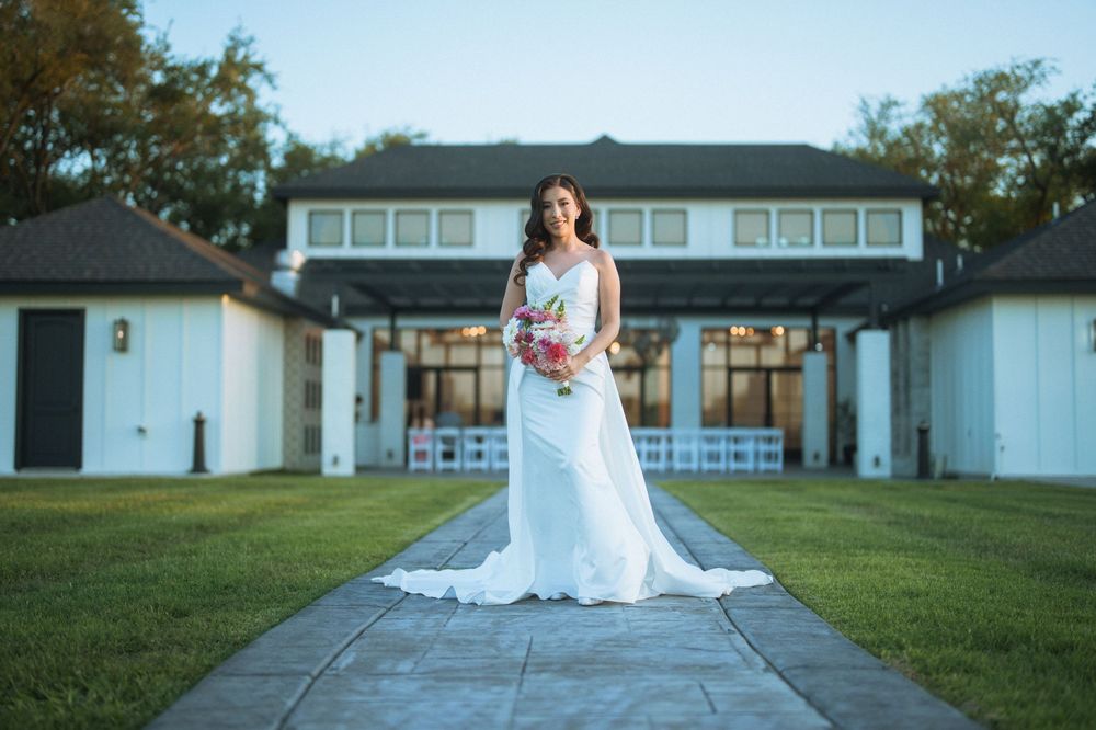A bride poses in an elegant white gown in front of a stately building with columns.