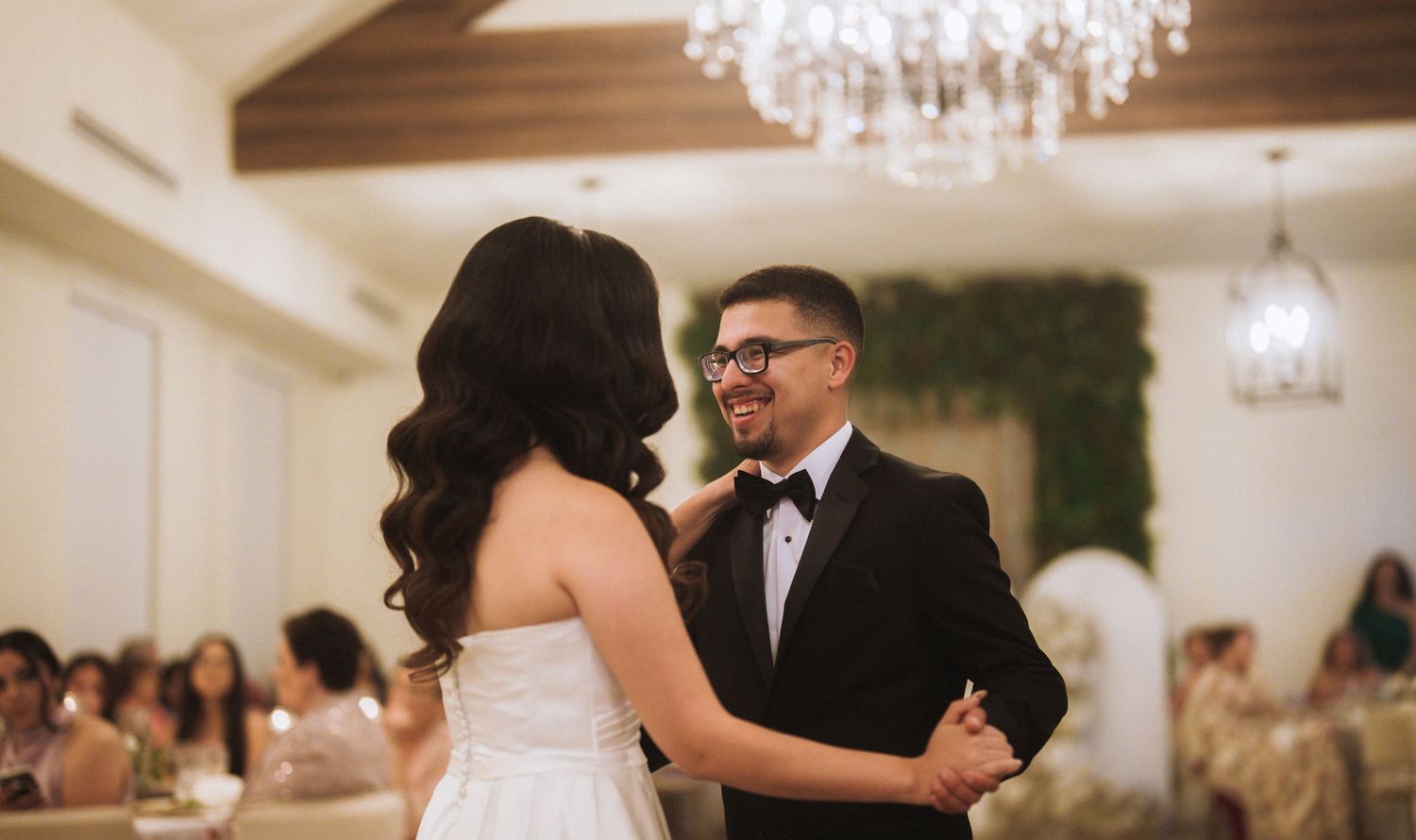 Elegant wedding reception venue with crystal chandeliers and couples dancing on a polished wood floor.