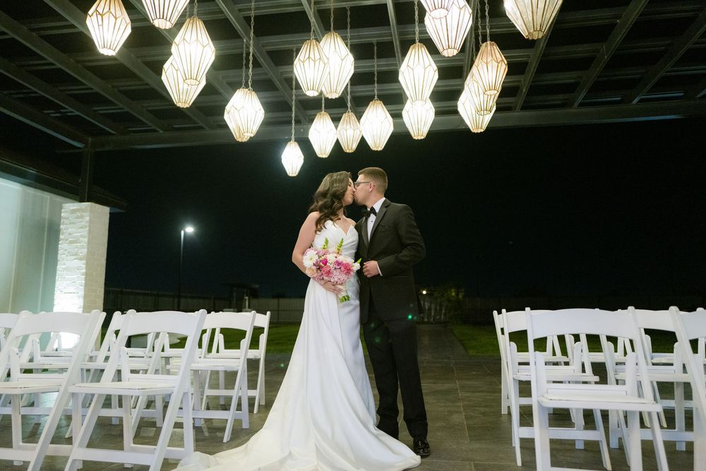 Outdoor evening wedding ceremony setup with white chairs and hanging lantern lighting.
