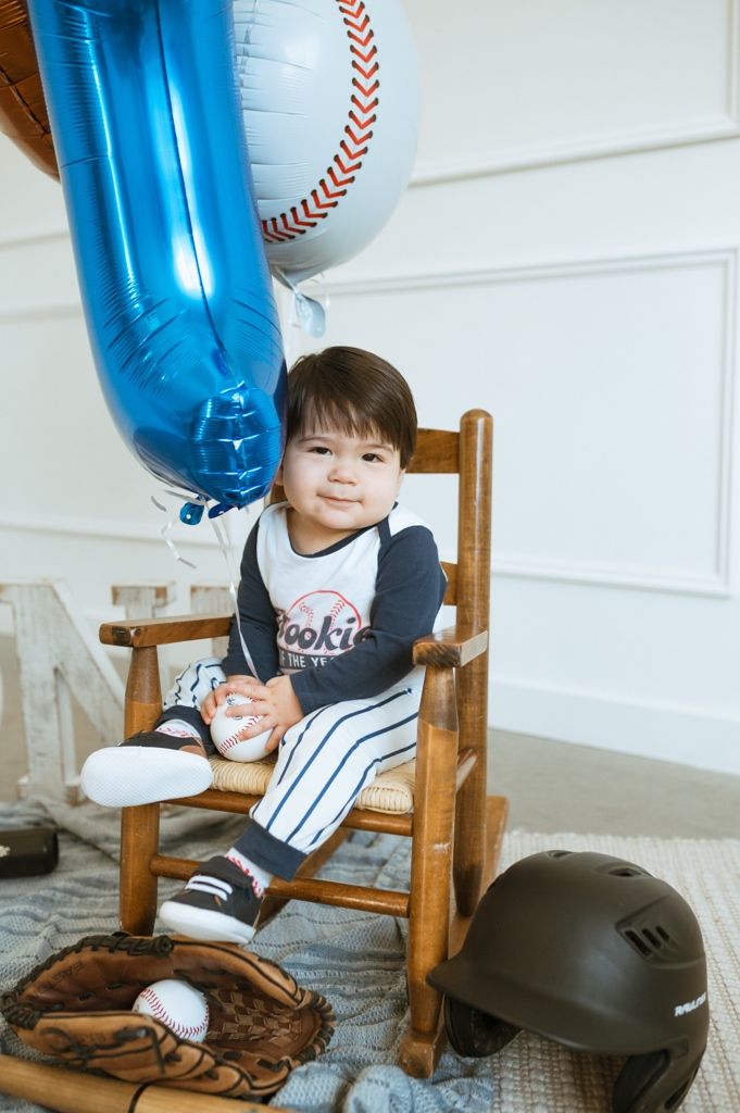 Baseball themed photoshoot setup with a blue number balloon and wooden rocking chair.