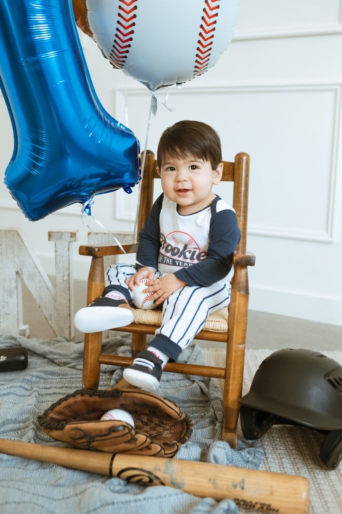 Baseball themed setup with wooden bat, glove, and blue balloon decorations on gray carpet.