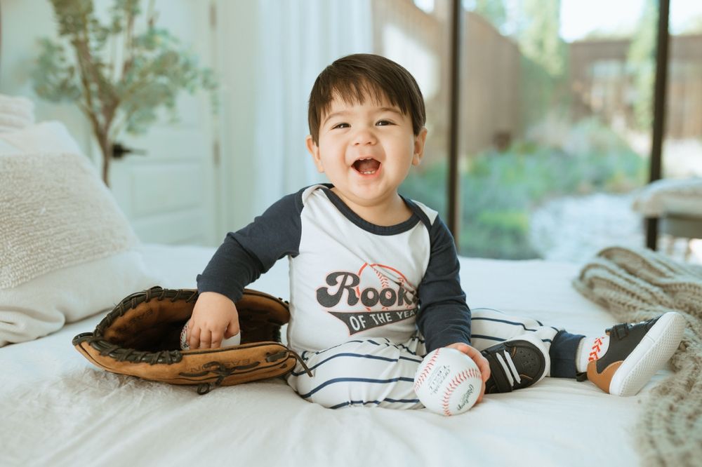 Baseball themed nursery setting with white bedding and decorative baseball elements.