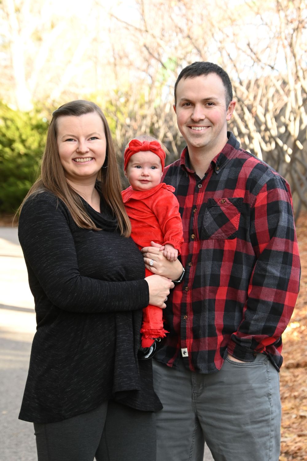 A family in coordinated black and red buffalo plaid outfits poses together outdoors during a fall photo session.