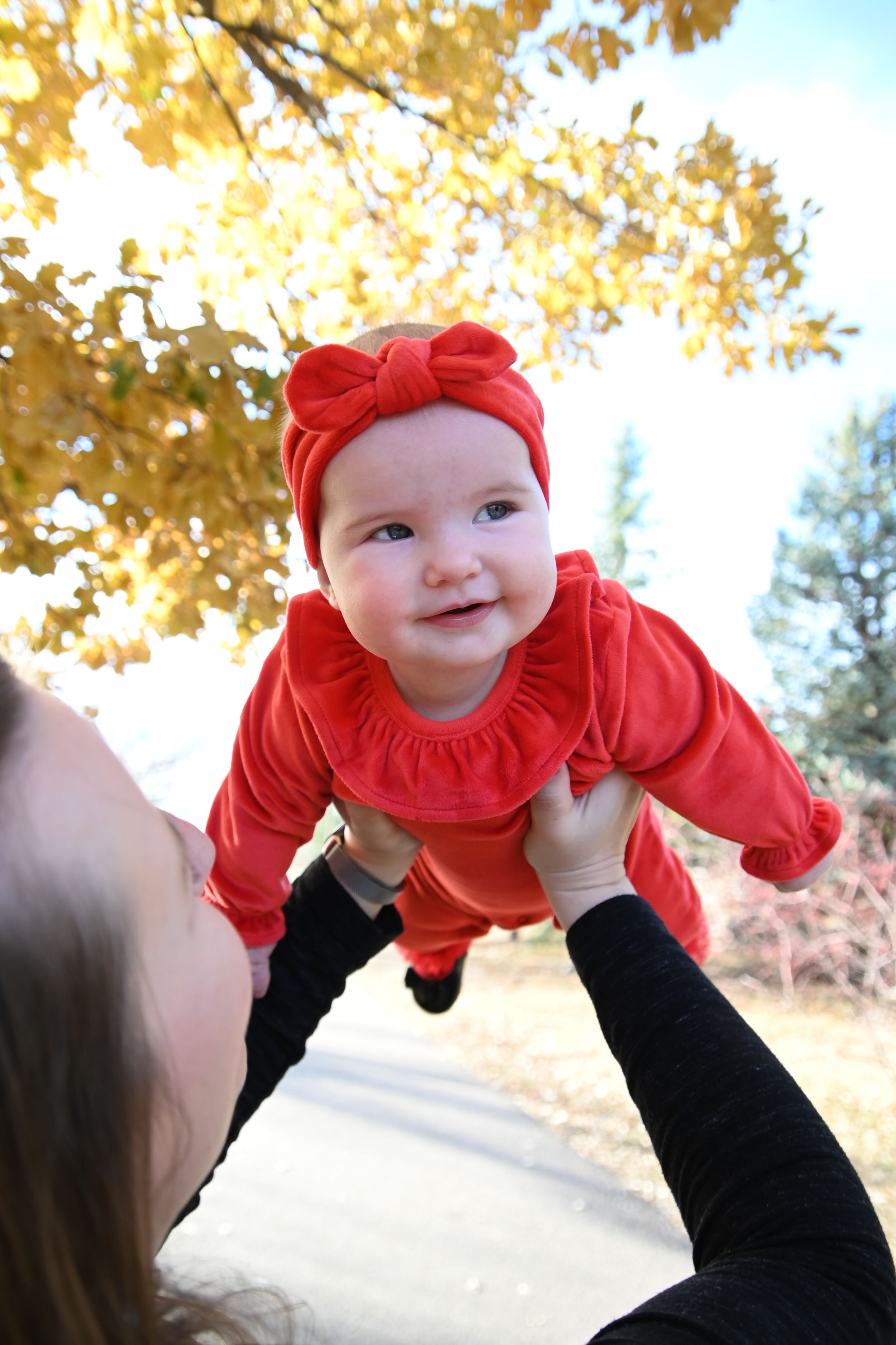 A series of five photos showing a small baby in a red outfit being lifted up against a fall backdrop with golden leaves.