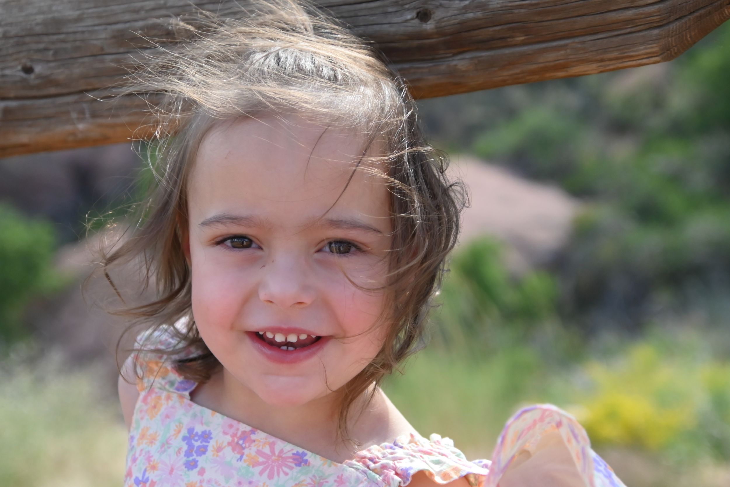 A happy child with windblown hair smiles brightly on a sunny day outdoors.