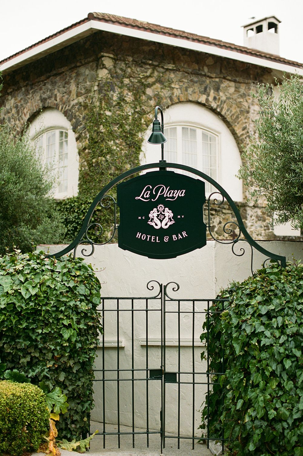 La Playa Hotel entrance sign mounted on stone wall with decorative iron gate and greenery.
