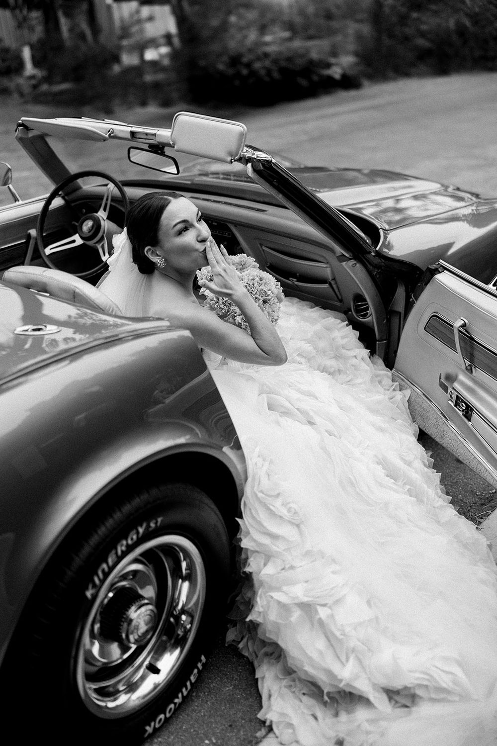 Dramatic black and white photos of a wedding dress flowing over a vintage convertible car.