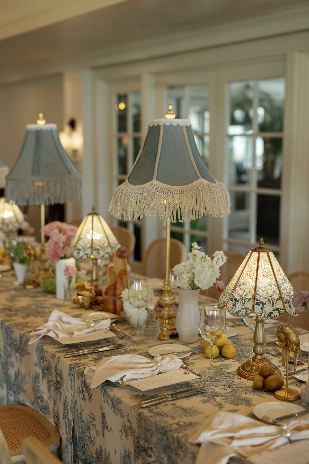 Elegant table settings with blue toile tablecloths and vintage-style table lamps create a romantic dining atmosphere.