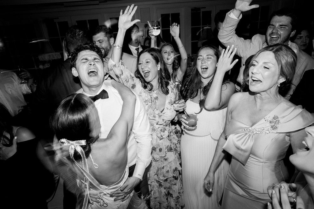 Wedding reception guests dancing and celebrating with hands in the air in black and white.