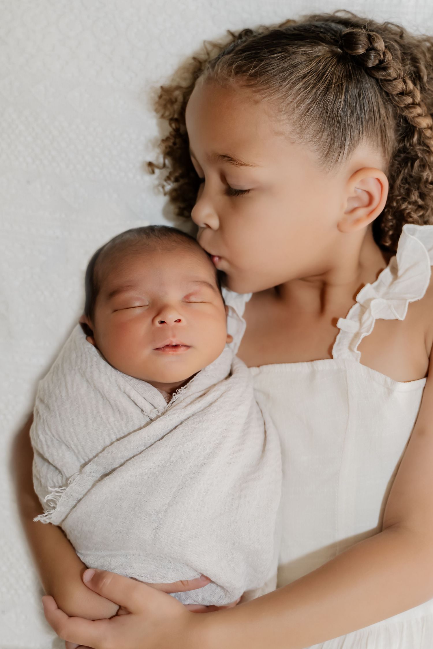 Tender moment captured in black and white as siblings share a gentle embrace on white bedding.