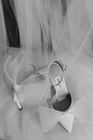 Elegant white bridal shoes with ankle straps rest on delicate tulle veil in black and white photography.