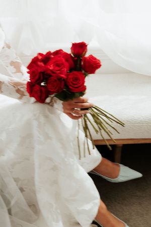 A white-clad figure holding a vibrant bouquet of red roses against a light background.