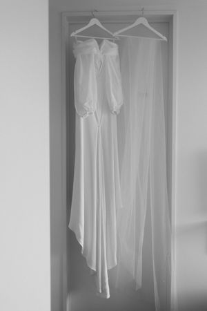 A series of white dresses and garments hanging in a row on wooden hangers against a light background.