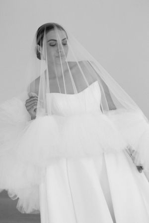 Black and white portrait of a bride wearing a flowing tulle veil and strapless ball gown wedding dress.