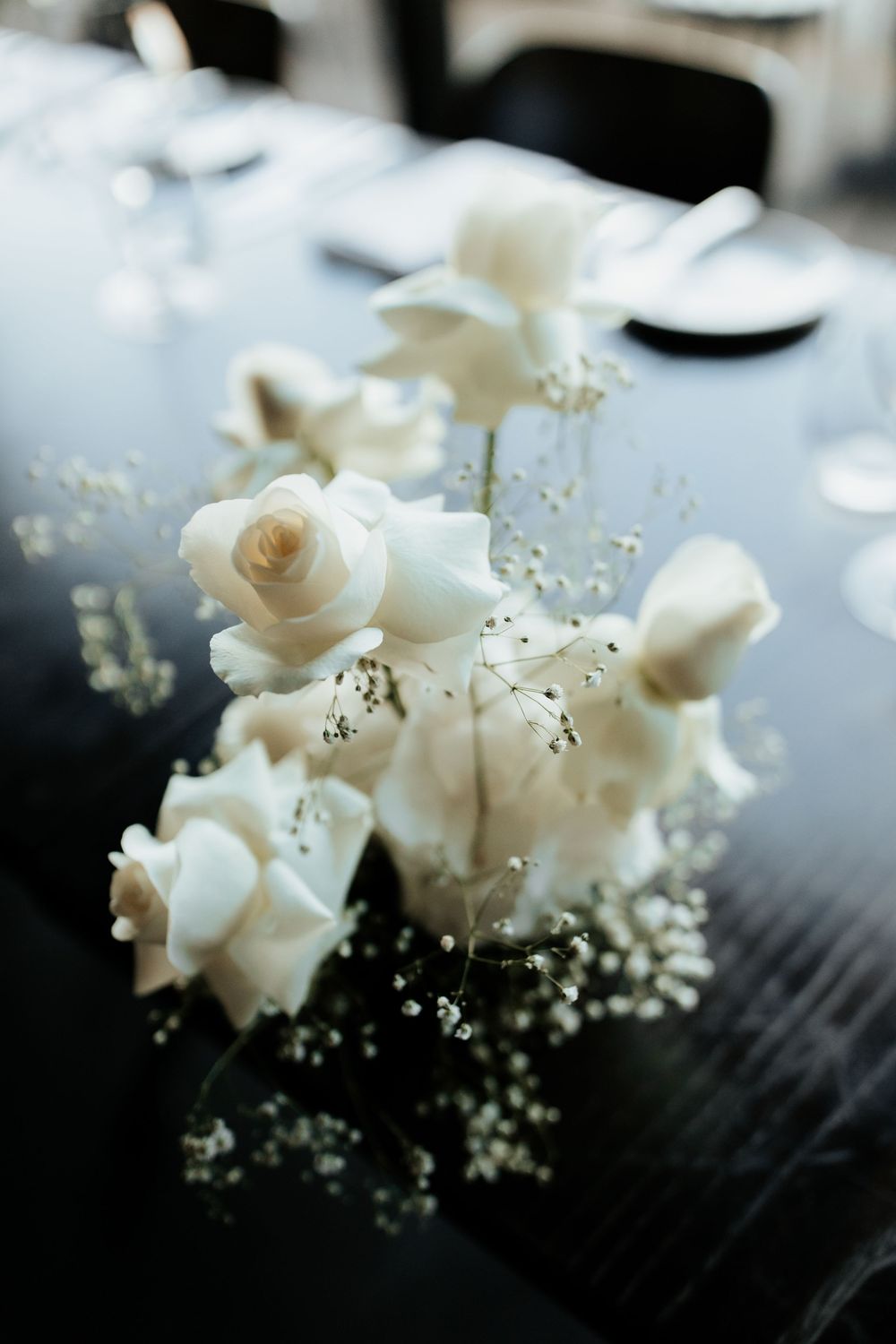 A delicate arrangement of white roses and baby's breath flowers in soft focus against a dark background.