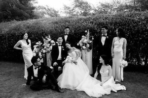 Wedding party members gather for formal outdoor portrait photographs in lush garden setting.