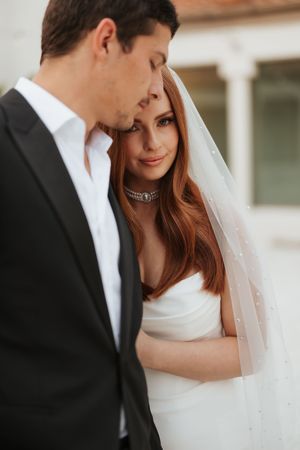 Intimate wedding portrait featuring couple in elegant black and white attire with romantic veil details and soft lighting.