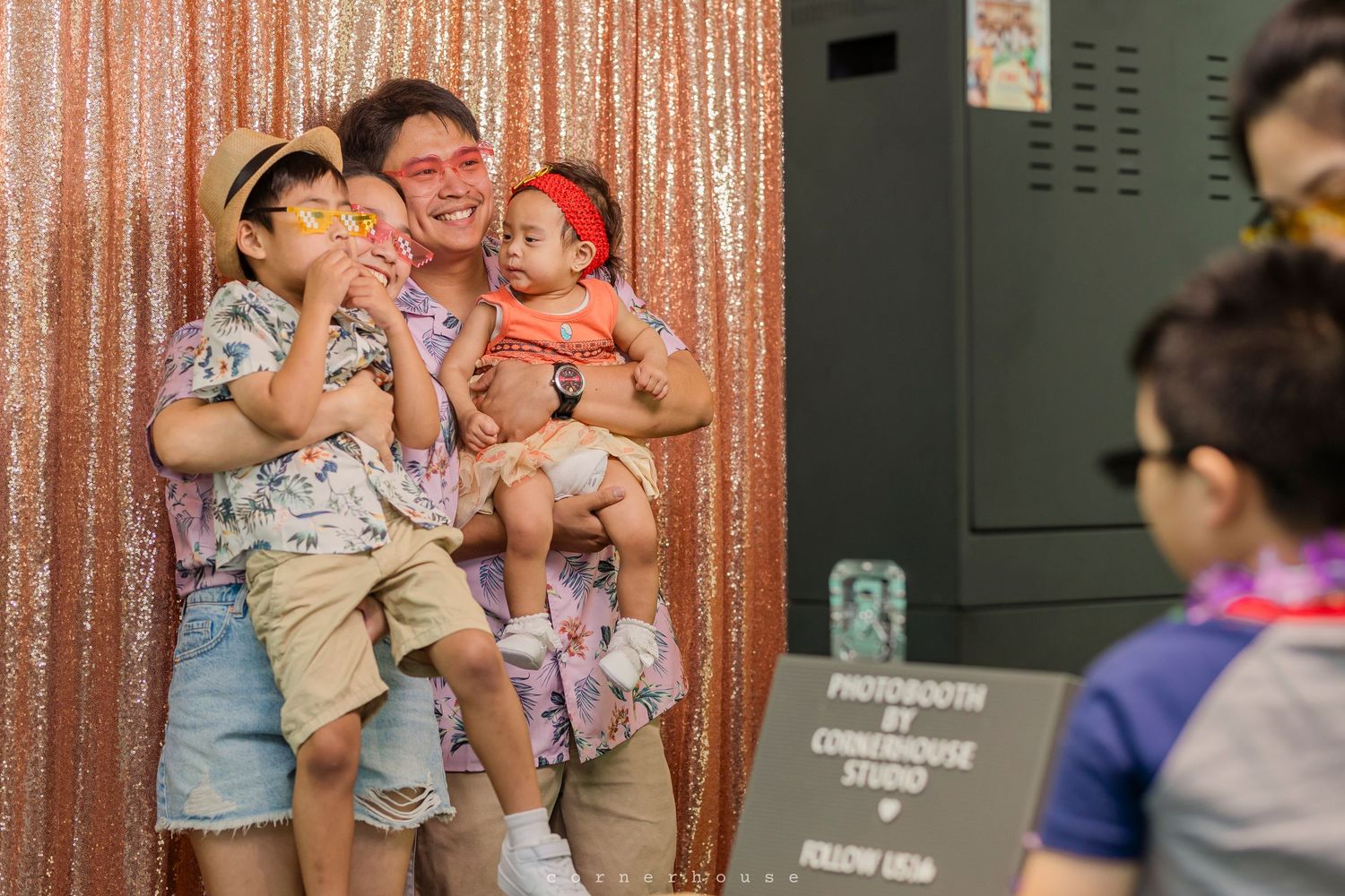 People stand in front of a rose gold sequin backdrop during a photo booth session at an event.