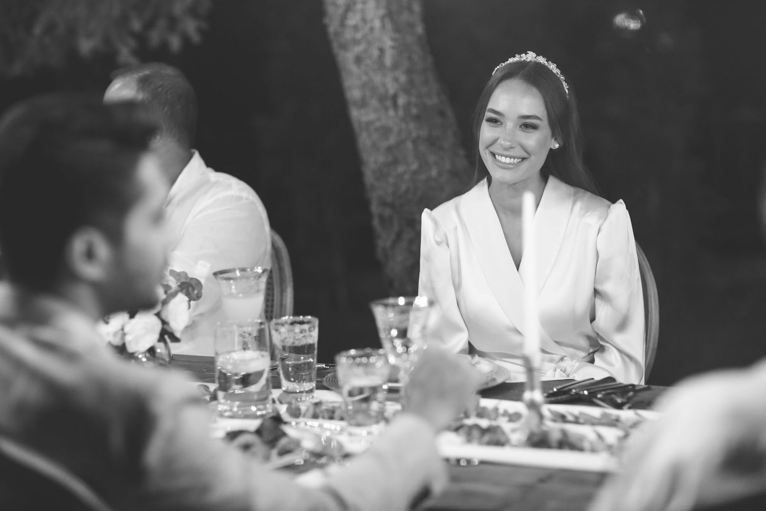 Black and white image shows wedding reception dinner guests seated at a table enjoying a meal and conversation.