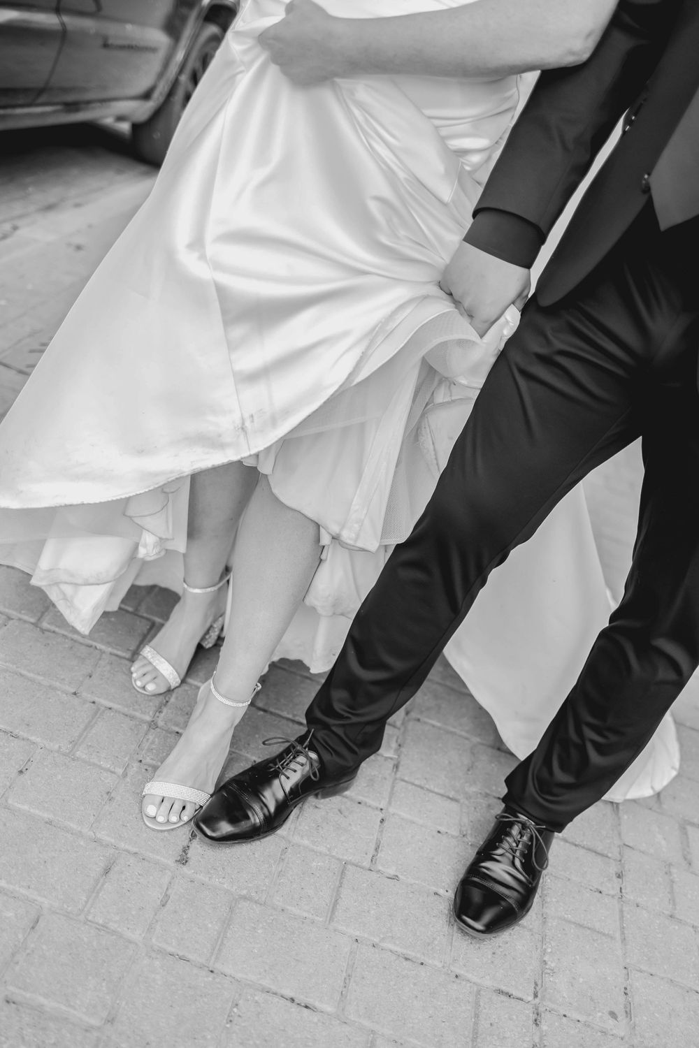 Black and white photo showing contrasting wedding shoes and formal attire on a brick pathway.
