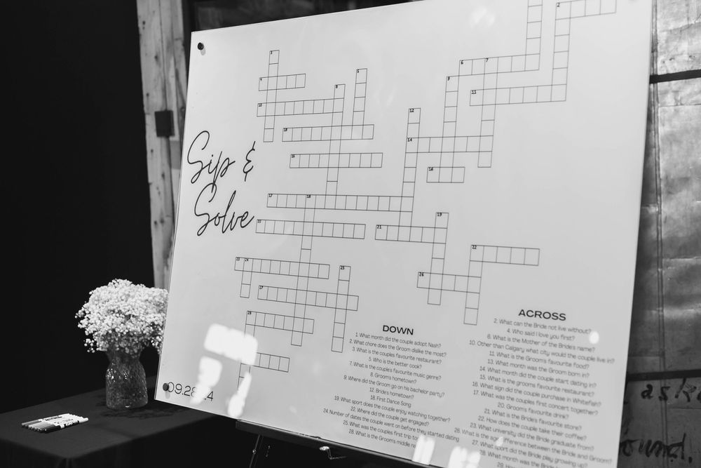 A black and white photograph shows a crossword puzzle board with text and grid displayed against a wall.