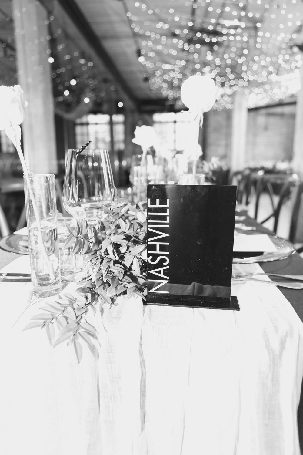 Wedding reception table settings with elegant glassware, black name cards and twinkling lights in the background.